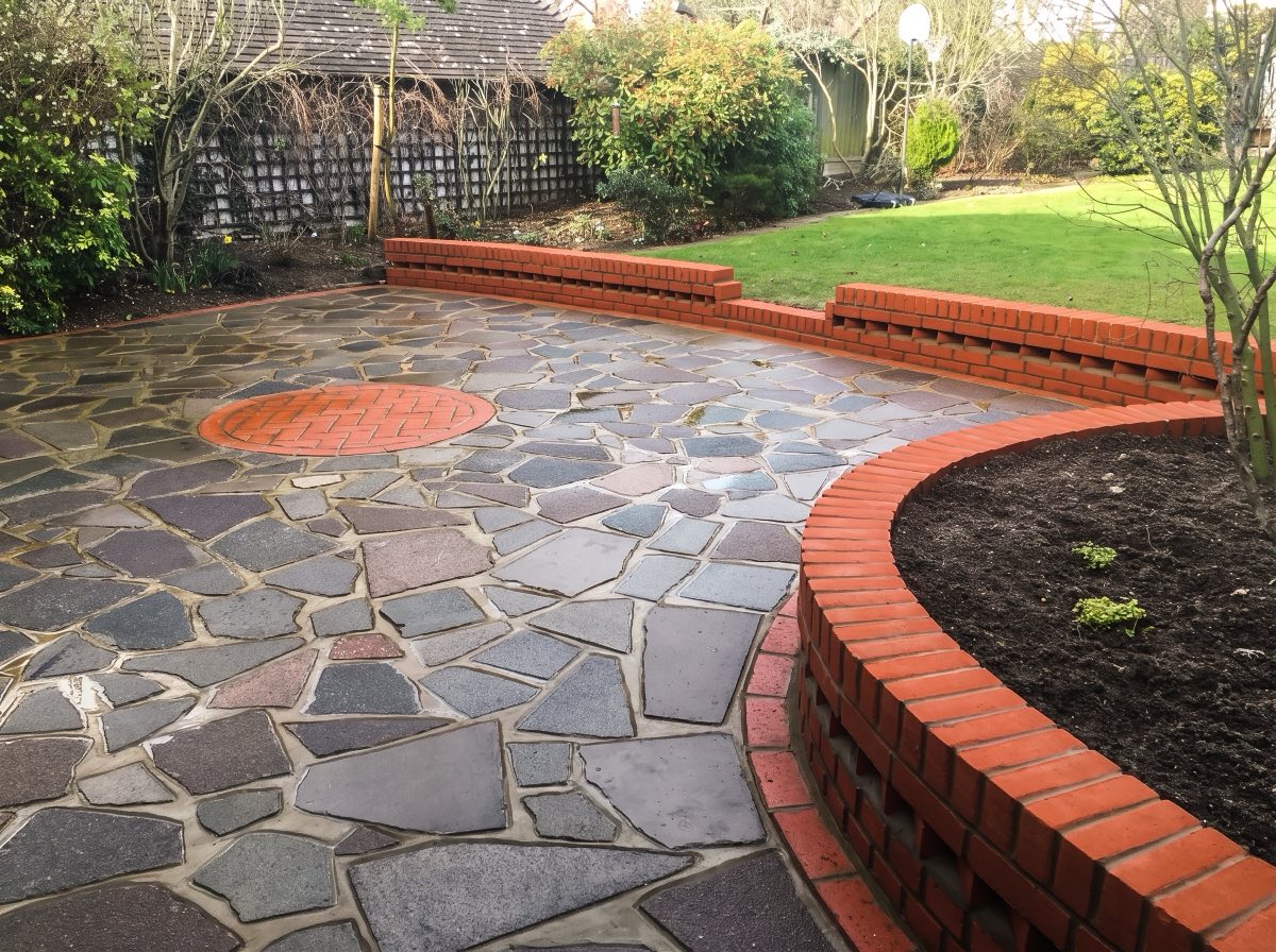 Crazy paving patio with a red brick circle and curved brick raised beds