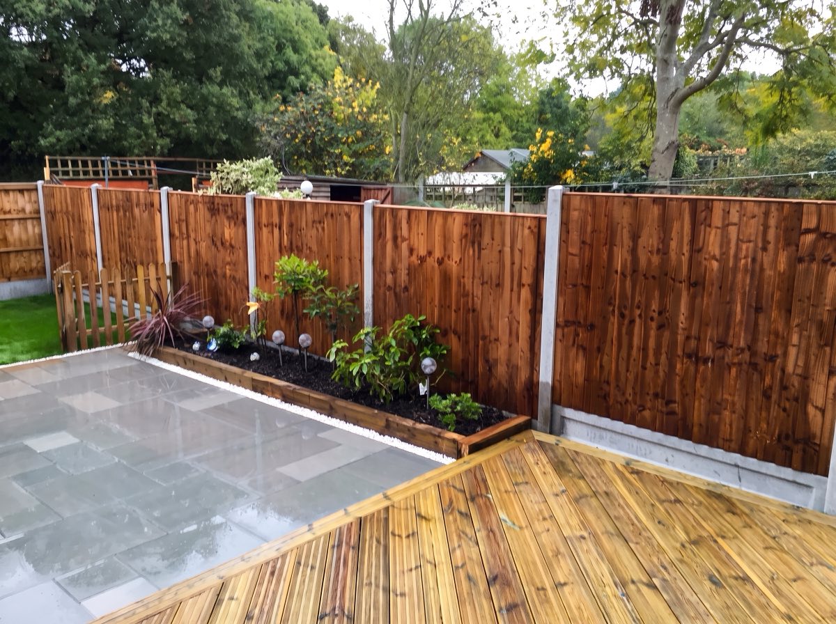 Grey slab patio beside timber decking with a planted sleeper bed