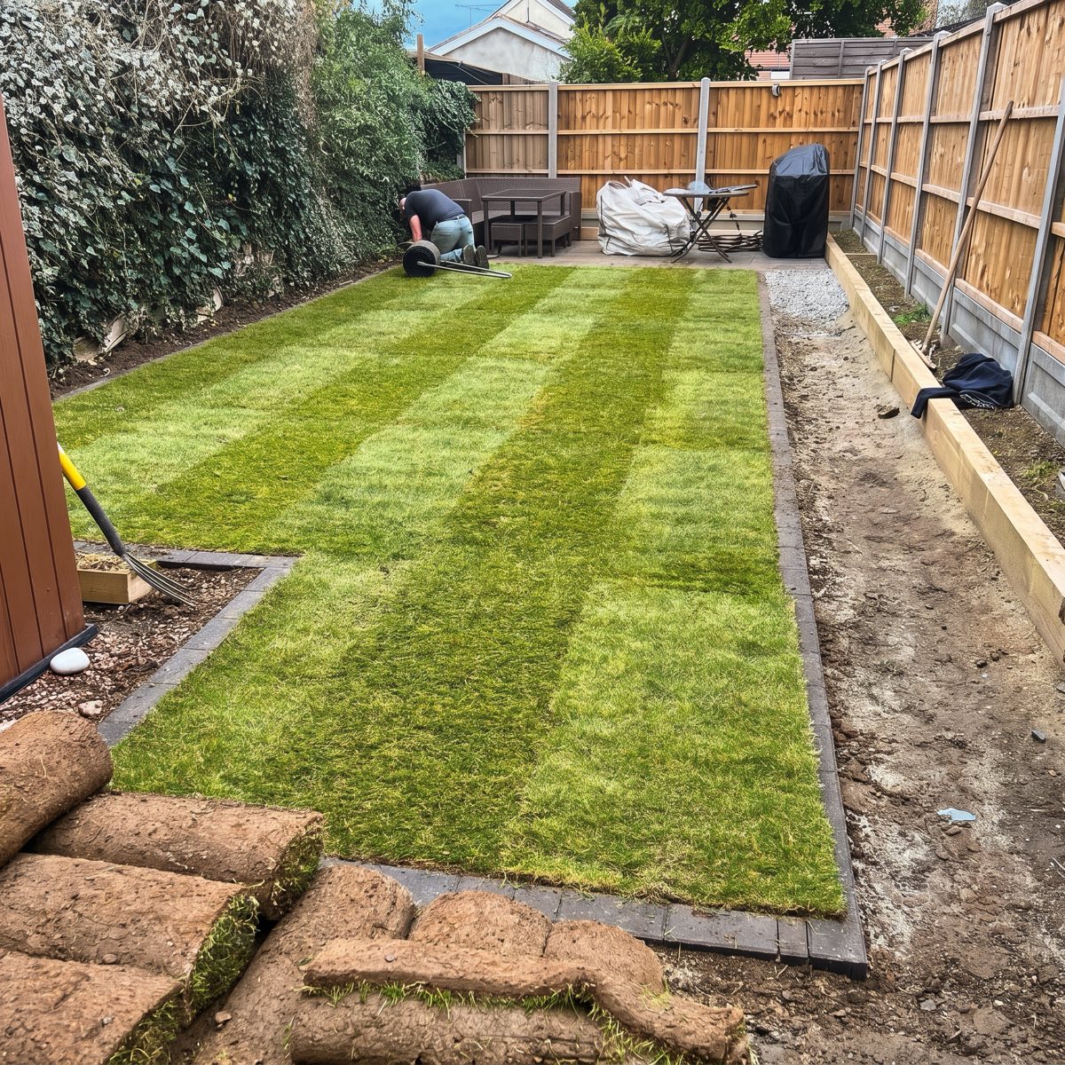 New striped turf being laid inside block edging, turf rolls in the foreground