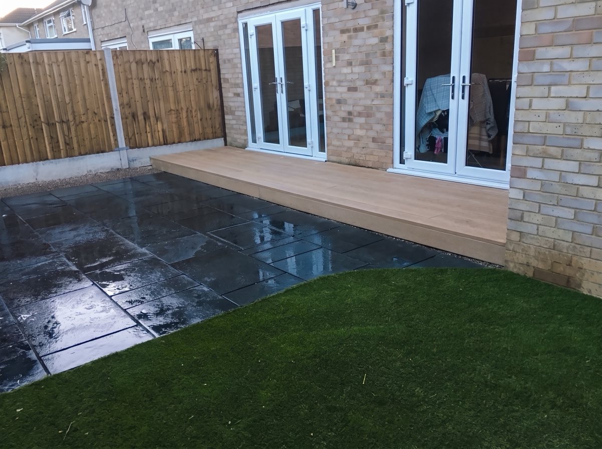 Dark slab patio with a composite decking step and artificial lawn